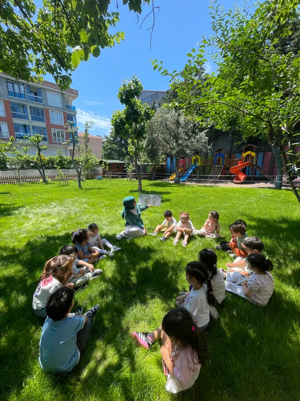 Ağaçların altında çim oyun alanı ve ahşap park